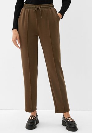 Bruine sweatpants met een trekkoord in de taille, zijzakken en een rechte pijpdesign, gecombineerd met zwarte instapschoenen met een gouden kettingaccent.