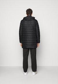 Svart, quiltad puffjacka med huva, långa ärmar och rak skärning. Bärs över svarta byxor och vita sneakers. Slät textur.