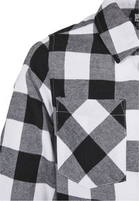 Camisa de cuadros en blanco y negro con un diseño de botones en la parte frontal, cuello y un bolsillo con parche en el lado izquierdo. La tela tiene un tejido texturizado.