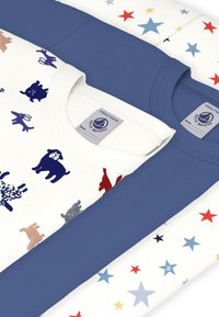 Trois t-shirts pliés : un bleu marine, et deux à motifs — blanc avec des étoiles colorées, et crème avec des imprimés d'animaux en bleu et rouge.
