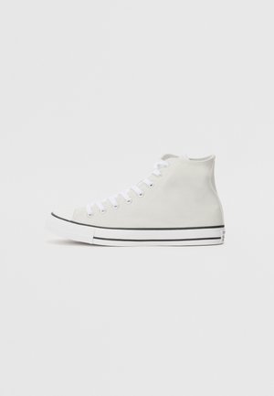 Witte canvas hoge sneaker met witte veters en zwarte strepen op de witte rubberen zool, zijwaarts weergegeven tegen een effen achtergrond.