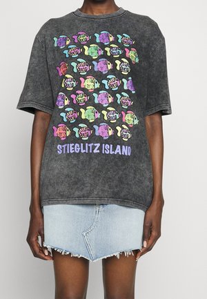 T-shirt oversize tie-dye noir avec un imprimé coloré de poisson et le texte "STIEGLITZ ISLAND" en bas. Confectionné en coton doux.