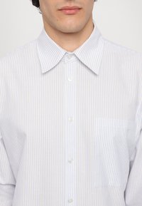 Camicia a button-up in blu chiaro e bianco a righe, realizzata in cotone. Presenta un colletto a punta, cinque bottoni e una tasca sul petto lato sinistro.