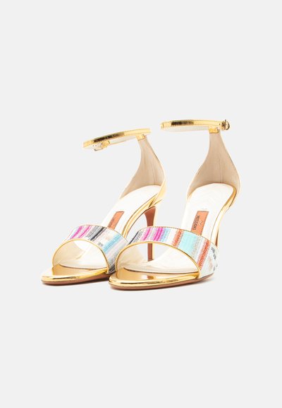 Para sandałów na wysokim obcasie z odkrytymi palcami, ze złotymi paskami wokół kostki i wielokolorową, paskowaną tkaniną na palcach.
