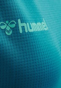 Turkos atletisk tröja med texturerad tyg och vertikala ränder. Anmärkningsvärd märkning med "hummel" och en logotyp i en kontrasterande nyans.