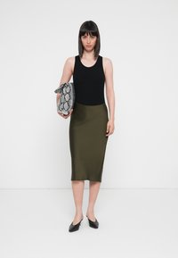 Black sleeveless top, olive green pencil skirt, black flat shoes, and a textured snake print clutch with a bow tie detail. Plain background.