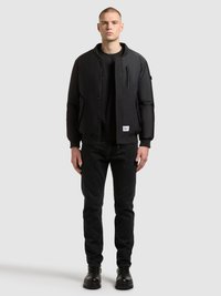 Czarna kurtka typu bomber z wysokim kołnierzem, napami, kieszeniami na zamek i ściągaczami przy mankietach, zestawiona z czarnymi dżinsami i czarnymi butami.