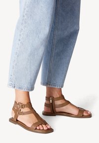 Bruna sandaler med remmar och öppen tå-design, med dragkedja och dubbla spännen, tillsammans med ljusblå avklippta jeans.