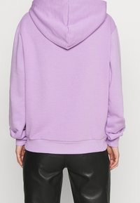 Lila Kapuzenpullover mit großer Kapuze, gerippten Bündchen und Saum. Kombiniert mit schwarzen Lederhosen. Weiche, glatte Textur mit minimalen Nähten.