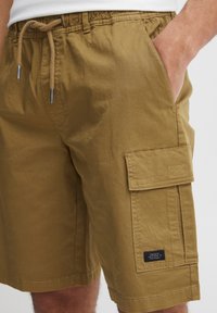 Khaki cargo shorts made of lightweight fabric, featuring an elastic waistband with drawstring, side pockets, and a large cargo pocket.