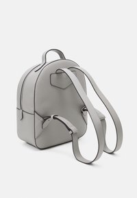 Vaalea harmaa muotoleather-reppu, jossa on pyöreä muoto, säädettävät olkahihnat, pääkahva ja hillityt mustat reunat.