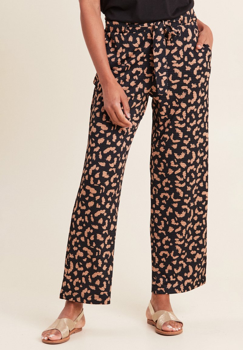 Zijde-brede broek in zwarte stof met een lichtbruine dierenprint, voorzien van een trekkoord in de taille en zijzakken. Gecombineerd met metallic sandalen.