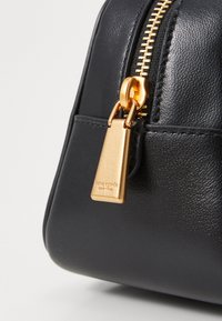 Black leather handbag with a smooth texture, featuring a gold zipper and hardware details. The zipper pull has a rectangular gold tag.