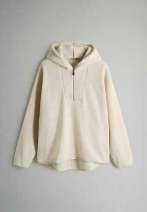 Kermainen fleece-pullover, jossa on vetoketjullinen puolikiinnitys, huppu ja pitkät hihat. Pehmeä rakenne ja pyöristetty helma alareunassa.