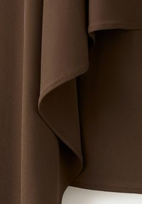 Primo piano di tessuto tessile marrone scuro con bordi piegati sovrapposti e dettagli di cucitura visibili.