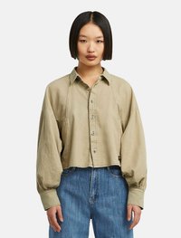 Camicia beige cropped con colletto strutturato e maniche lunghe e voluminose. Tessuto morbido con una vestibilità rilassata e dettagli di cucitura sottili.
