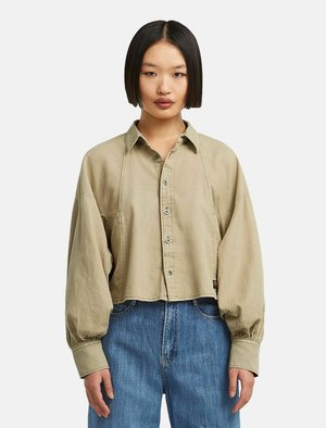 Camicia beige cropped con colletto strutturato e maniche lunghe e voluminose. Tessuto morbido con una vestibilità rilassata e dettagli di cucitura sottili.