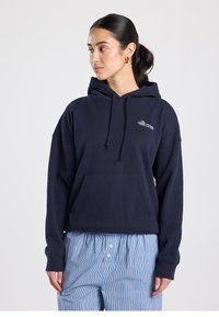 Sweat à capuche bleu marine en tissu doux, avec une poche avant, des cordons de serrage et un logo brodé. Associé à un pantalon rayé bleu.