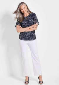 Navy blouse met witte stippen, korte mouwen, ronde hals met sleutelgatdetail, gecombineerd met witte flarebroek en navy wedge hakken.