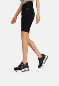 Gonna di denim nera con orlo sfrangiato e design attillato, abbinata a sneaker nere con accenti lucidi e suola a righe bianche.