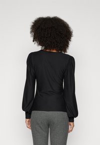 Black long-sleeve top featuring puffed sleeves, a fitted silhouette, and a smooth texture. Paired with textured houndstooth pants.