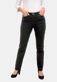 Jeans en denim noir ajustés, avec cinq poches, fermeture à bouton sur le devant et une texture lisse, associés à des chaussures à talons hauts noires.