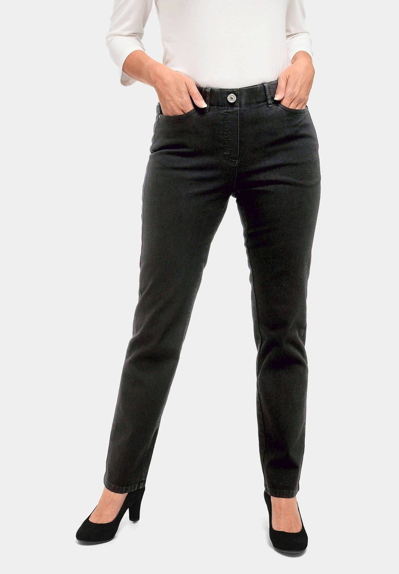 Jeans en denim noir ajustés, avec cinq poches, fermeture à bouton sur le devant et une texture lisse, associés à des chaussures à talons hauts noires.