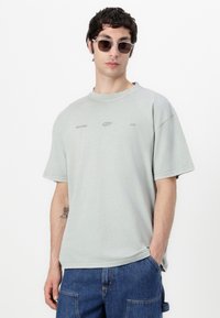 Lichtgroene oversized t-shirt met korte mouwen, ronde halslijn en subtiele branding. Draag het met een zonnebril; gecombineerd met donkere spijker shorts.