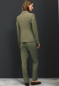 Olivově zelený přizpůsobený oblek se strukturovaným sakem a slim-fit kalhotami, s hladkou texturou a jemnými švy.