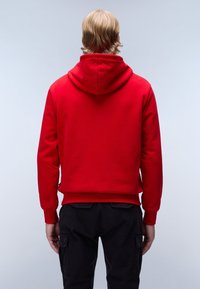 Rode capuchontrui gemaakt van zachte stof. Voorzien van een kangoeroezak en geribbelde zoom en manchetten. Eronder worden donkere broeken gedragen.