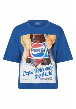 Niebieska koszulka z grafiką dłoni trzymających butelkę Pepsi otoczoną lodem oraz napisem "Pepsi wita świat."