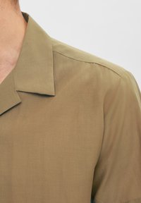 Kortärmad skjorta i olivgrön, med en avslappnad krage och ett mjukt, strukturerat tyg med subtil lyster och rena sömdetaljer.