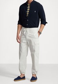 Granatowa koszula zapinana na guziki, pasiasty podkoszulek, białe spodnie bojówki z wiązaniem w talii oraz granatowe espadryle. Materiały: bawełna, swobodny krój.