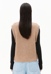 Gebreid sweater-vest met een beige lijf en geribbelde zwarte mouwen. Heeft een losse pasvorm en neutrale tinten, geschikt om over elkaar te dragen.