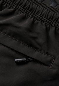 Pantaloni corti neri in tessuto con vita elasticizzata, dotati di una tasca con zip e un'etichetta "SUPERDRY". Texture liscia, design semplice.