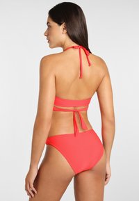 Ensemble de bikini rouge comprenant un haut à nouer derrière le cou et un bas offrant une couverture moyenne. Tissu lisse et extensible avec un minimum de coutures.