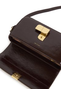 Sac bandoulière en cuir marron foncé avec fermoir en métal doré, poche zippée à l'intérieur et sangle ajustable sur fond blanc.