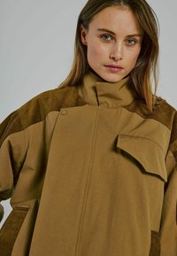 Braune Baumwolljacke mit Cord-Details, hohem Kragen, übergroßer Passform, Knopfverschluss und einer Fronttasche. Glatte Textur.