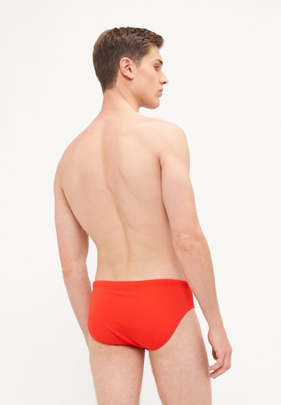 Rote Badeunterhosen aus glattem Stoff, mit einem tiefen Schnitt, schlichtem Design und minimalen Nähdetails.