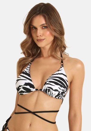 Kobieta z falującymi brązowymi włosami, ubrana w czarno-biały top bikini z zebrowym nadrukiem i czarnymi paskami owijającymi na jednolitym tle.