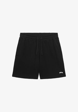 Schwarze, gerippte Strickshorts mit elastischem Bund, Kordelzug, seitlichen Taschen und kleinem weißem "UNFAIR"-Logo am linken Bein.
