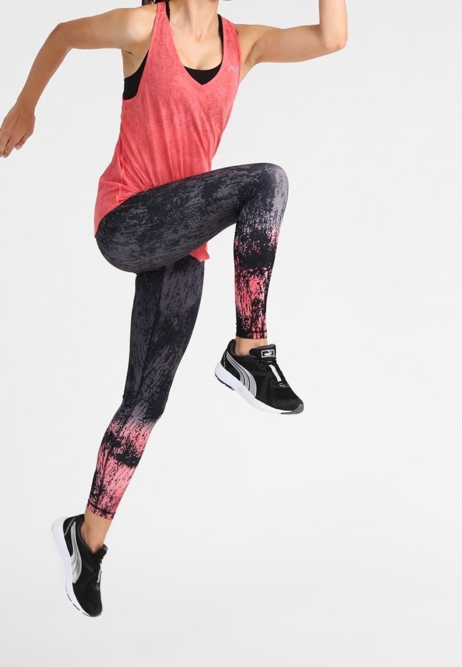 Czerwona bluzka bez rękawów, legginsy w czarno-różowy wzór i czarne buty sportowe z białymi podeszwami. Strój przeznaczony jest do aktywności fizycznej.