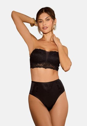 Vrouw in een zwart kanten strapless bh en hooggeplaatste onderbroek, poseert met de ene arm omhoog en de andere hand op haar nek.