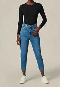 Černý top s dlouhým rukávem ve spojení s modrými džíny s vysokým pasem, které mají rovný střih, doplněné bílými teniskami.