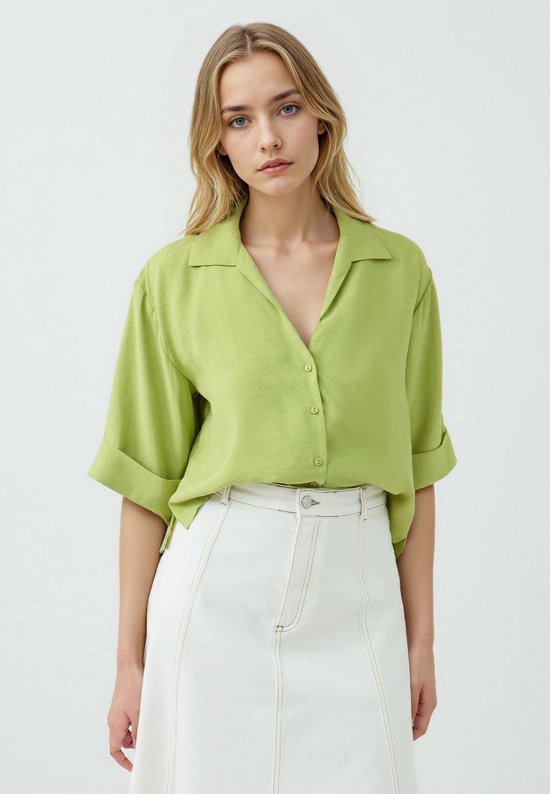 Camicia button-up verde lime a maniche corte con colletto, in tessuto liscio e dal taglio rilassato, abbinata a una gonna bianca a vita alta.