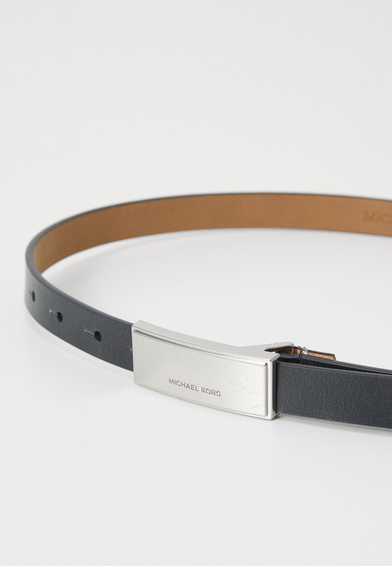 Cintura in pelle di un blu scuro con fodera interna marrone, dotata di una fibbia metallica rettangolare incisa con "Michael Kors". Texture liscia.