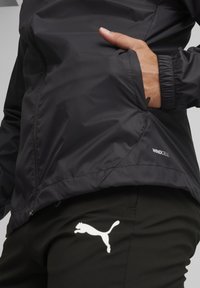 Schwarze leichte Windjacke mit Mesh-Innenfutter, mit Reißverschluss ausgestattetem Taschen und elastischen Bündchen. Enthält ein "WINDCELL"-Etikett und das Puma-Logo auf den Hosen.