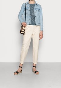 Chaqueta de mezclilla, blusa azul con estampado, pantalones beige ajustados y sandalias de esparto negras. Bolso bandolera a rayas negras y beige.