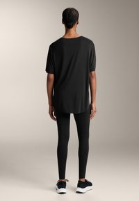 Musta lyhythihainen t-paita, jossa on kaareva helma, yhdistetty mustiin legginsseihin ja mustiin urheilukenkiin. Sujuva kangas, rento malli.