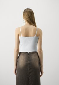 Top in cotone a coste di colore azzurro chiaro con spalline sottili, abbinato a una gonna in denim marrone a vita alta con una cerniera visibile sul retro.